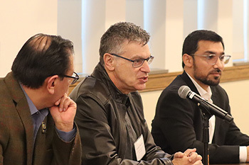 Three panelists at a table, Laurie Nathan speaking