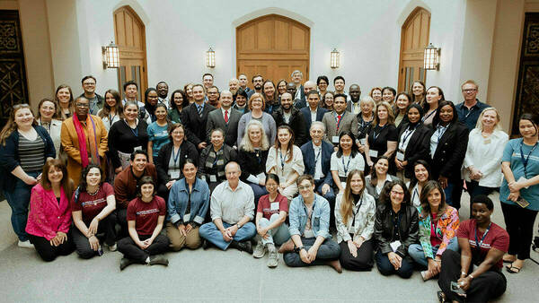 A diverse group of people posed indoors in front of a wooden door, suggesting a formal or conference setting.