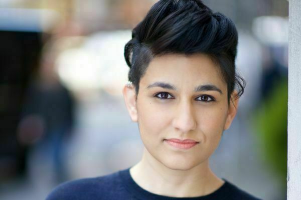 A woman with medium skin, dark eyes, and dark, short hair styled with volume on top looks forward with a subtle, pleasant expression. She wears a dark top against a blurred background.
