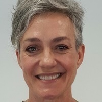 Woman with short gray hair smiles directly at the camera, showing teeth.