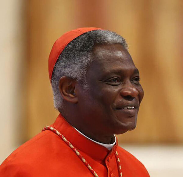 Cardinal Peter Turkson smiles, wearing a red cap and cassock.